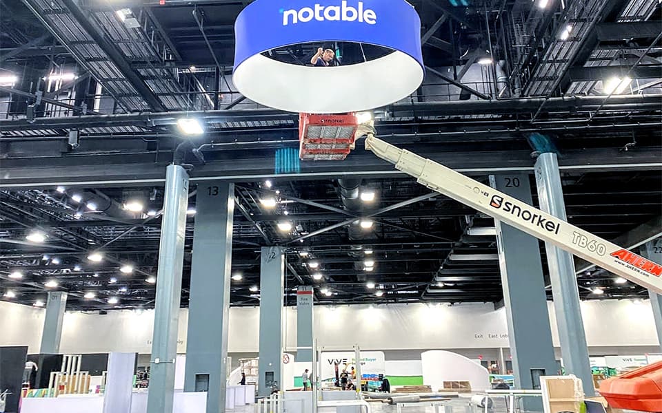 Crew in a boom lift installing a large hanging sign in a convention hall